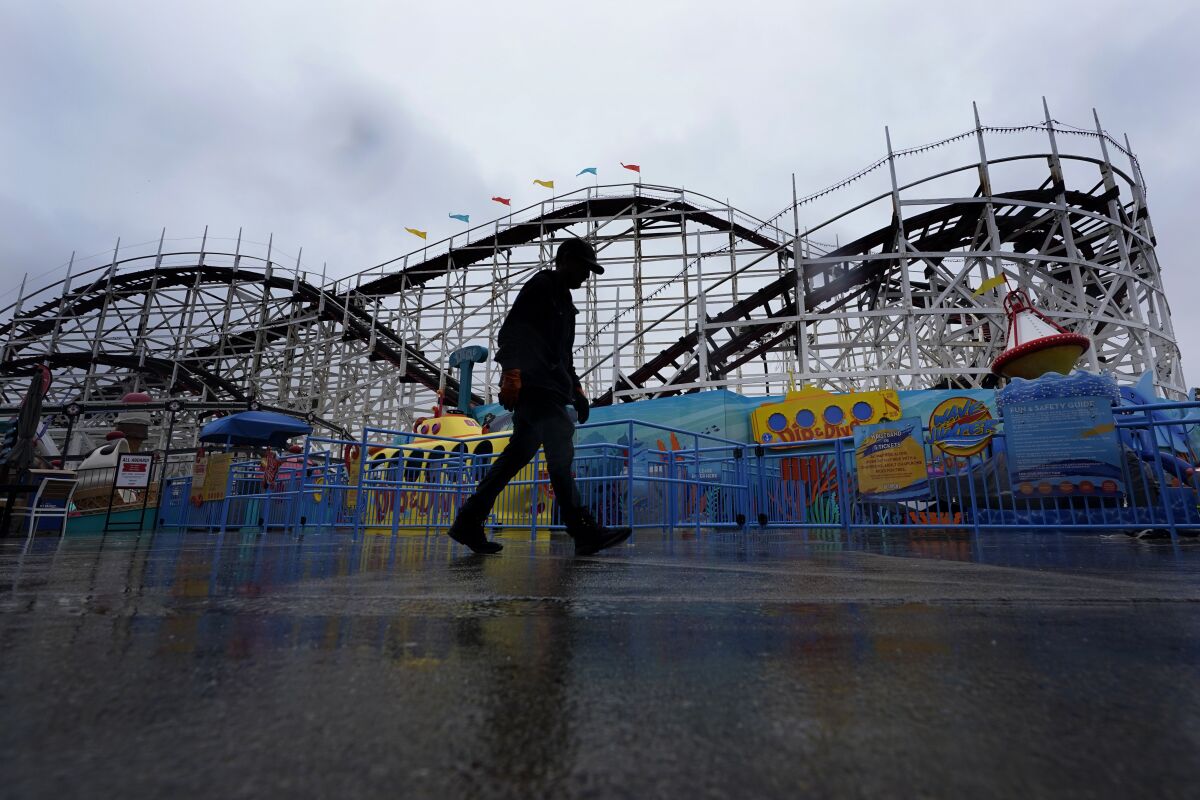 A worker passes the roller coaster at Belmont Park as rain engulfs the area, Tuesday, March 21, 2023, in San Diego. Californians are tired. Tired of the rain, tired of the snow, tired of stormy weather and the cold, relentlessly gray skies that have clouded the Golden State nearly nonstop since late December. (AP Photo/Gregory Bull)