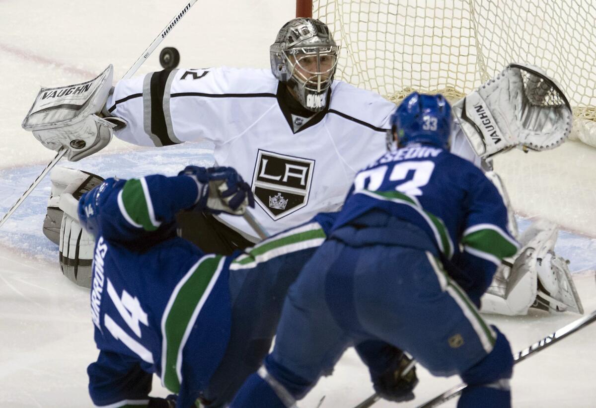 Kings goalie Jonathan Quick stops a goal despite having Canucks players Alex Burrows (14) and Henrik Sedin (33) right in front of him.