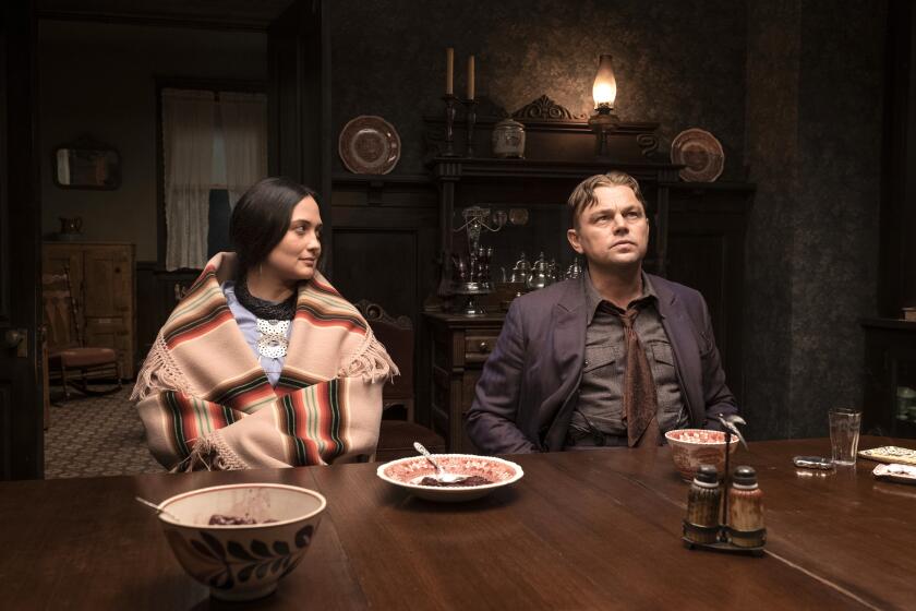 Lily Gladstone looks at Leonardo DiCaprio while seated at a dinner table in costume for the film 'Killers of the Flower Moon'