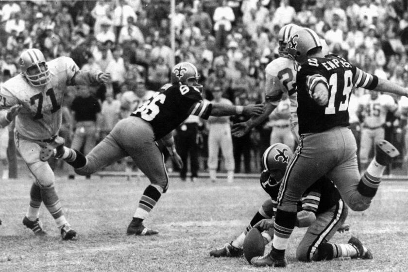 FILE - In this Nov. 8, 1970, file photo, New Orleans Saints' Tom Dempsey (19) moves up to kick a 63-yard field goal as teammate Joe Scarpati holds the ball and Detroit Lions' Alex Karras (71) rushes in while Saints' Bill Cody (66) blocks, in New Orleans. Dempsey, who played in the NFL despite being born without toes on his kicking foot and made a record 63-yard field goal, died late Saturday, April 4, 2020, in New Orleans while struggling with complications from the new coronavirus, his daughter said. He was 73 years old. (AP Photo/File)