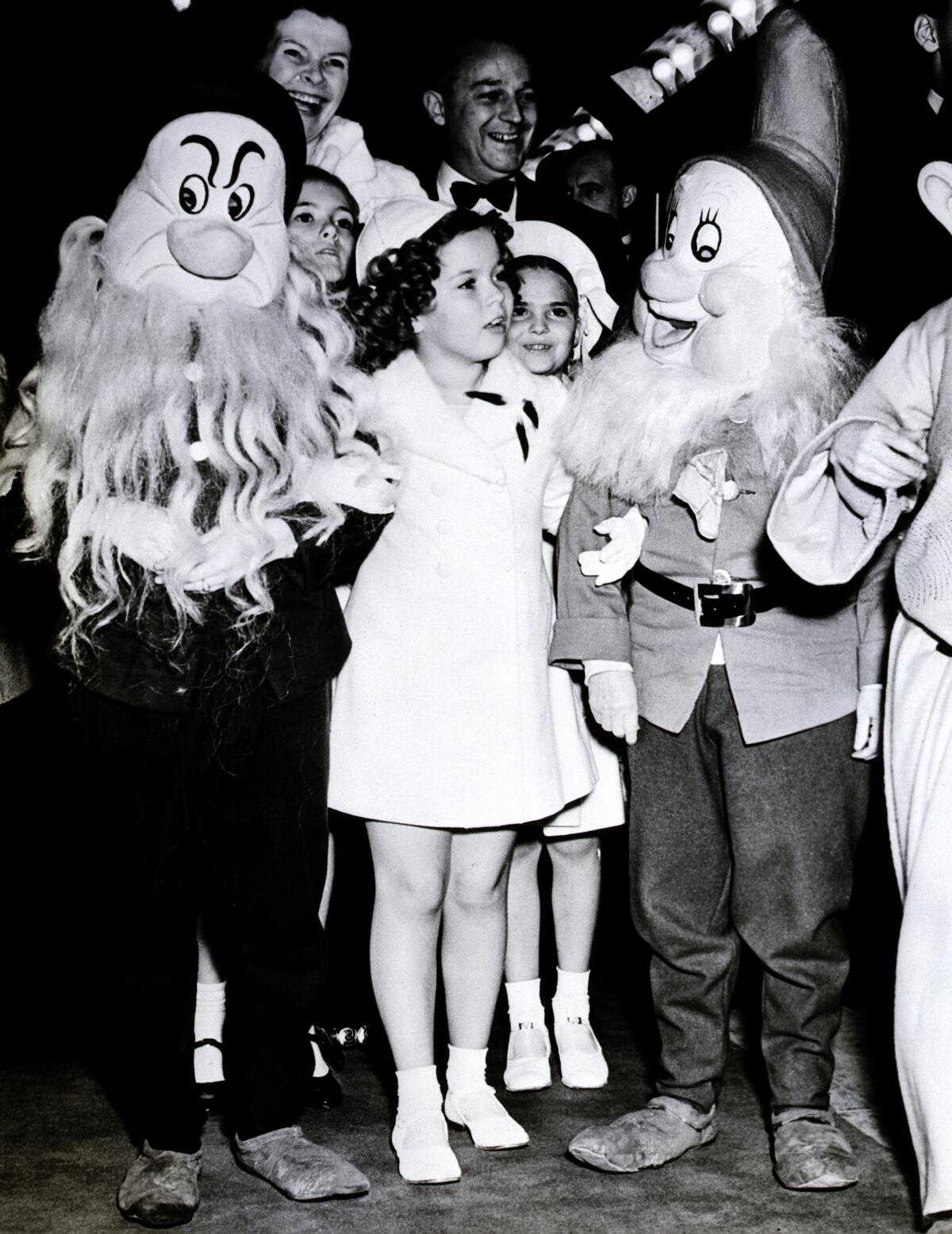 Shirley Temple stands with actors dressed as two characters from "Snow White and the Seven Dwarfs."