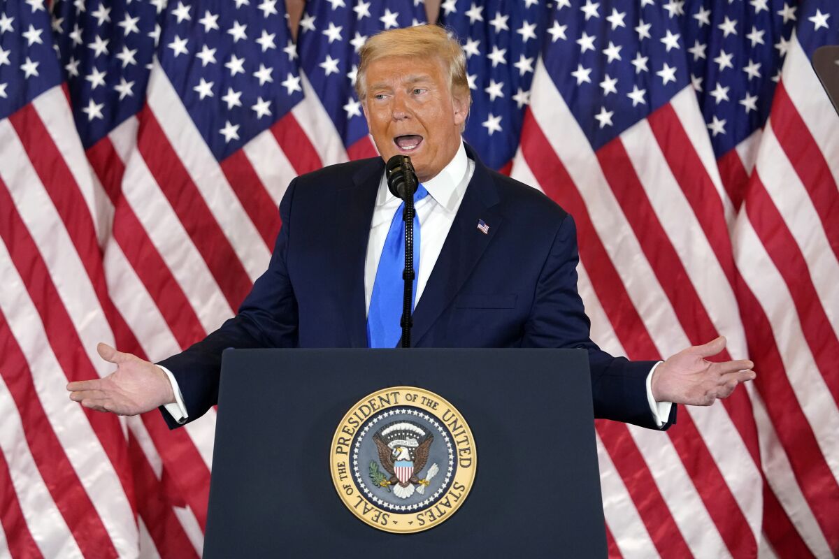 President Trump gestures with both hands while speaking at a lectern with the presidential seal in front of U.S. flags