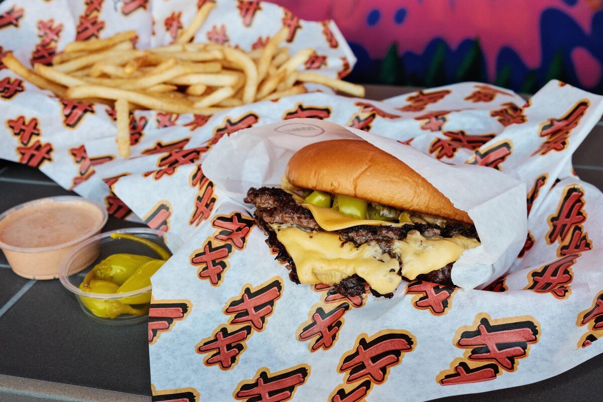 A close-up of a double cheeseburger with fries in branded paper at Heavy Handed in Studio City