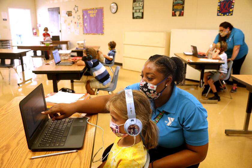 TORRANCE, CA - SEPTEMBER 17, 2020 - - Denecia Boone, a teacher with the YMCA, helps Maya Haldeman, foreground, with an exercise at the Anza Elementary School campus in Torrance on September 17, 2020. Anza Elementary School is one of many schools that are reformatting and rebranding as camps, enrichment programs and daycare, bringing students back to closed campuses for a fee. Torrance Unified School District is one of many that now offers fee-based, in person enrichment for its elementary school students, through the YMCA. (Genaro Molina / Los Angeles Times)