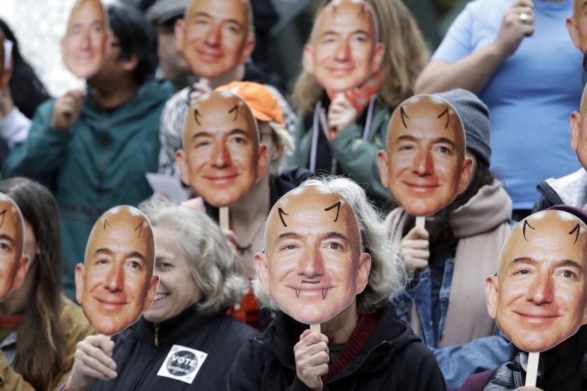 FILE - In this Oct. 31, 2018, file photo, demonstrators hold images of Amazon CEO Jeff Bezos near their faces during a Halloween-themed protest at Amazon headquarters over the company's facial recognition system, "Rekognition," in Seattle. San Francisco is on track to become the first U.S. city to ban the use of facial recognition by police and other city agencies as the technology creeps increasingly into daily life. Studies have shown error rates in facial-analysis systems built by Amazon, IBM and Microsoft were far higher for darker-skinned women than lighter-skinned men. (AP Photo/Elaine Thompson, File)