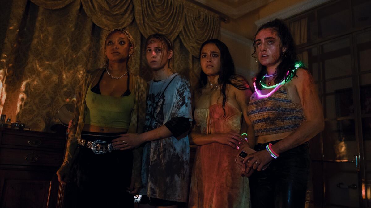 Four young women stand in a room looking scared.