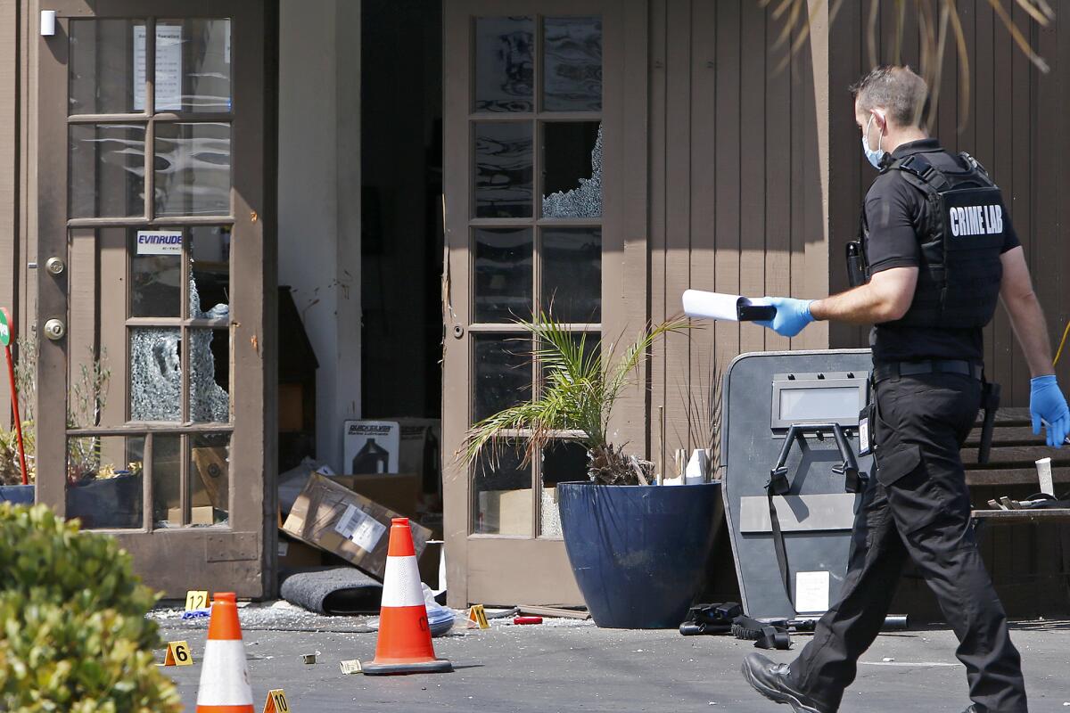 A crime lab investigator walks past a shattered doorway Wednesday at Advanced Marine Services in Costa Mesa. 