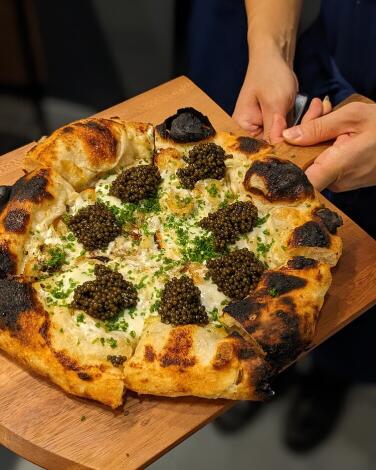 A hand holds a whole pizza, each slice topped with a mound of caviar