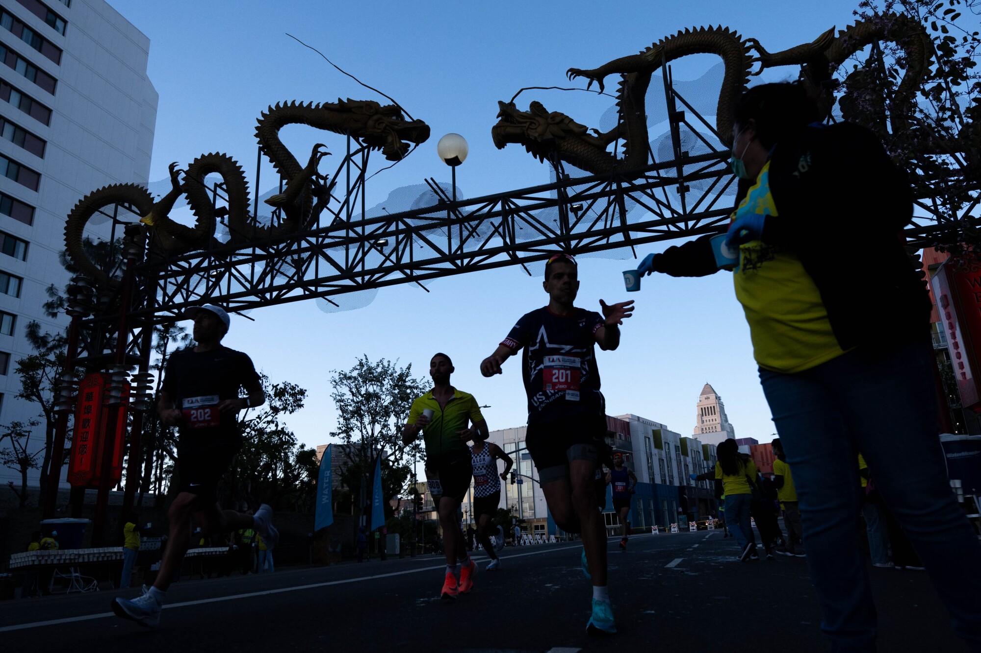 Runners pass under decorative dragons on a metal framework above a street.