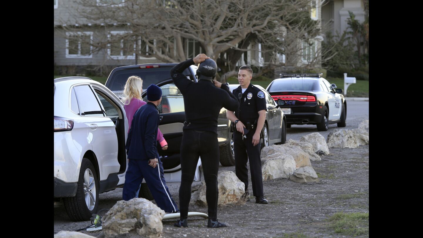 A Palos Verdes Estates police officer checks on outsider surfers Jordan and Diana Milena, left, and Cory Spencer, before they hit the waves at Lunada Bay in Palos Verdes Estates on Feb. 5, 2016.