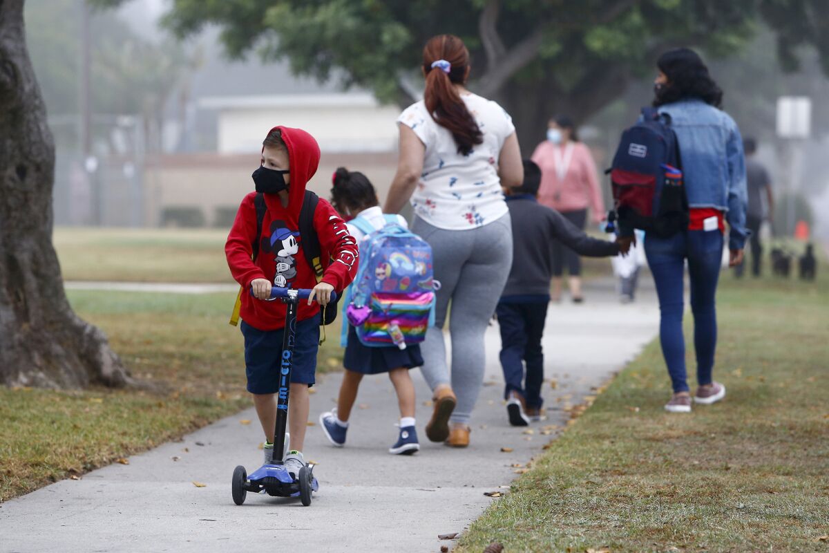A boy rides his scooter as students head to class at Rea Elementary School in Costa Mesa.