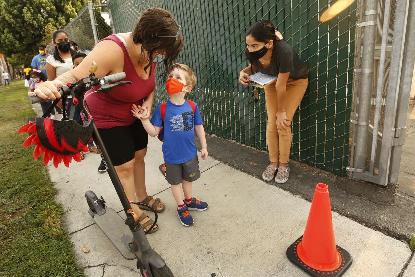 NORTH HOLLYWOOD, CA - AUGUST 17: Transitional Kindergartner Ryder White with mother Amber White checks in with Yazmin Magallon, Primary Promise Aide at Lankershim Elementary School in North Hollywood as parents and students check for the student name on a list using the Daily Pass website - designed to issue pre-approved health clearances for students to enter campus or present their QR code for entrance to the campus at Lankershim Elementary on Tuesday for the second day of in-class learning for LAUSD schools. "This is less chaotic today." Said Amber. The pre-approved health clearances for students to enter campus appeared to be up and working so the second day of school in the Los Angeles Unified School District appears to be going more smoothly than the first, largely devoid of the long lines and frustrations on back-to-school Monday when the district's student health-check system failed. Lankershim Elementary on Tuesday, Aug. 17, 2021 in North Hollywood, CA. (Al Seib / Los Angeles Times).