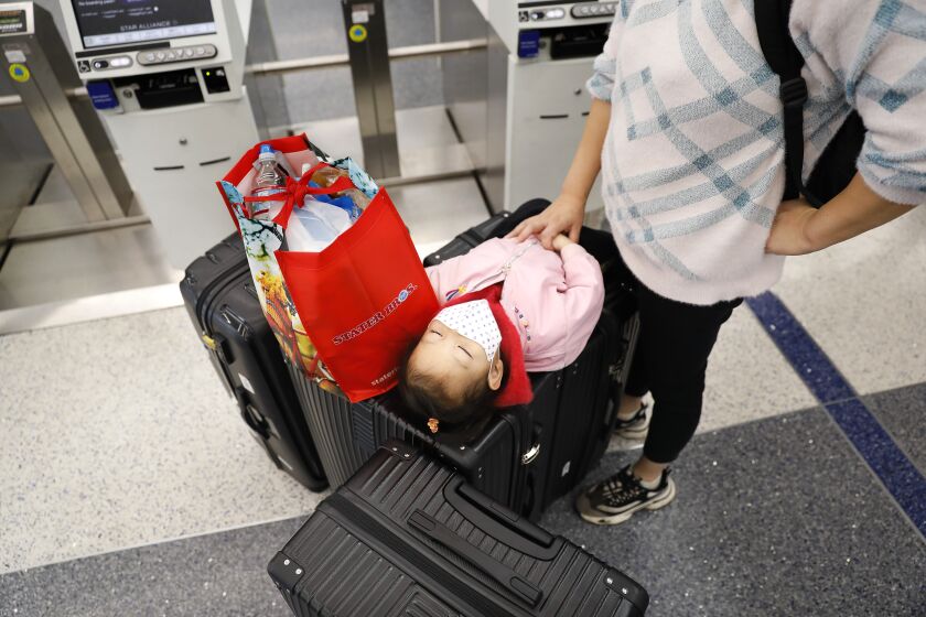 LOS ANGELES-CA-DECEMBER 27, 2021: A young traveler takes a rest on top of the family's luggage at LAX on Monday, December 27, 2021. At least 87 flights in or out of LAX were canceled Sunday, affecting some holiday travelers. (Christina House / Los Angeles Times)