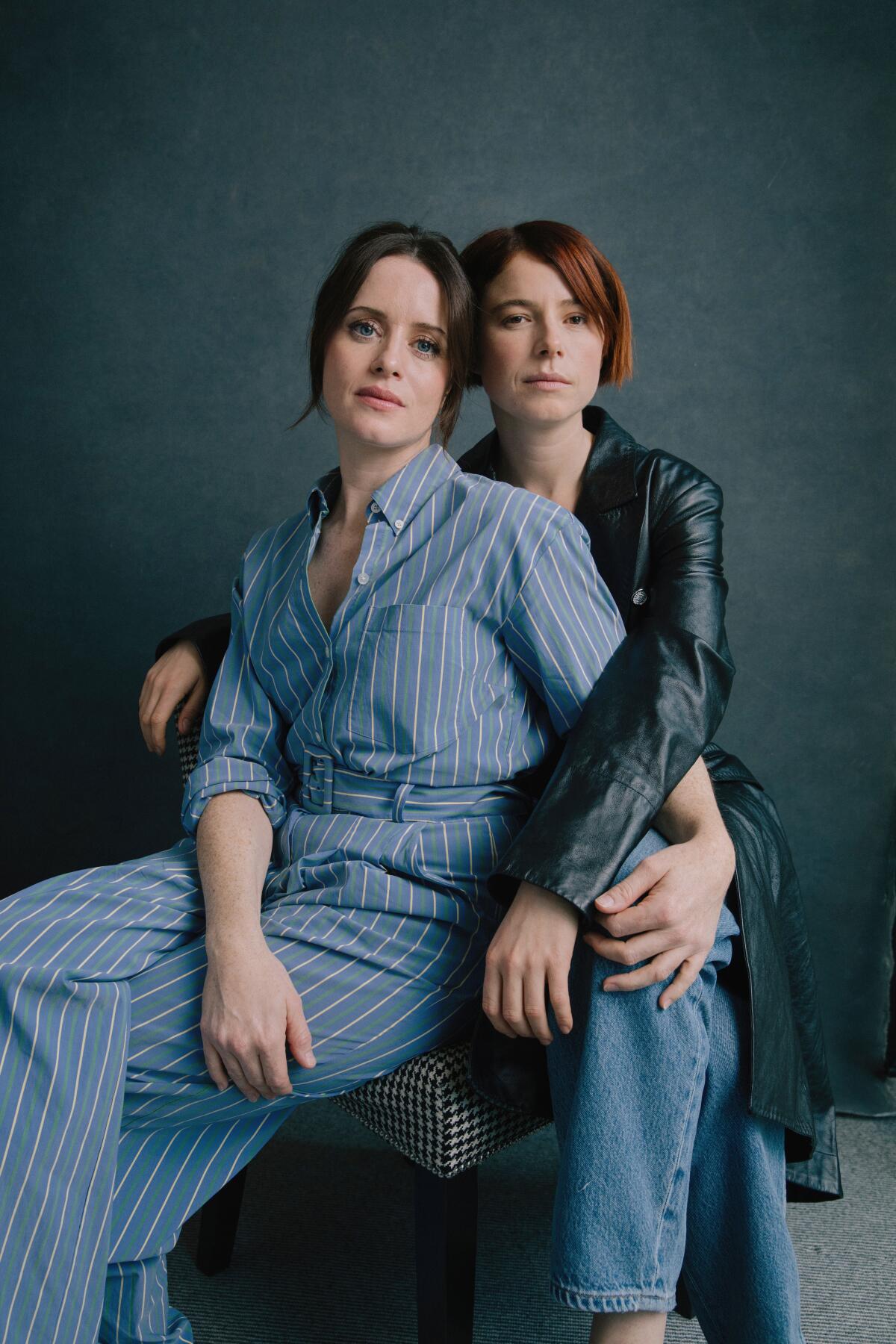 Two women sit, one behind the other, with their arms around each other