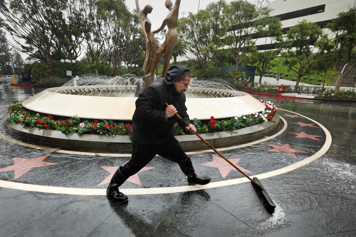 A man sweeps away water with a broom in front of a fountain with a statue in the center.