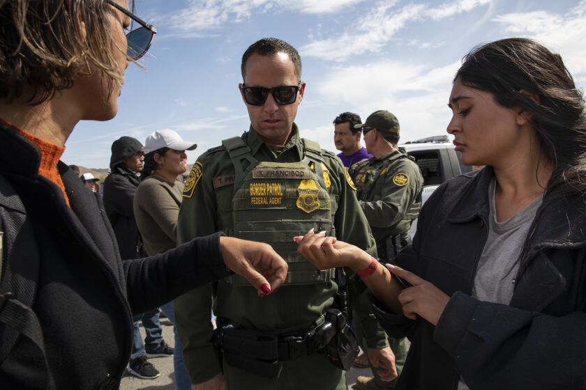 Jacumba , California - May 15: A woman from Brazil, left, and a woman from Colombia show their wrists bands to a Border Patrol agent to show how long they've been in a holding area on Monday, May 15, 2023 in Jacumba, California. Some people said they'd been in the area for six days. (Ana Ramirez / The San Diego Union-Tribune)