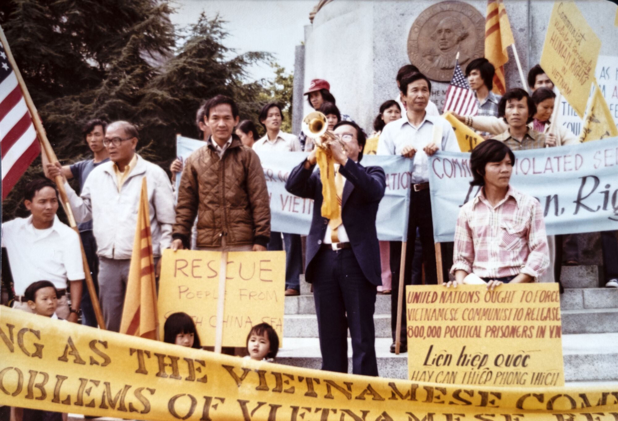 A 1979 photo shows Duc Tan next to a man playing a horn among a crowd at a rally