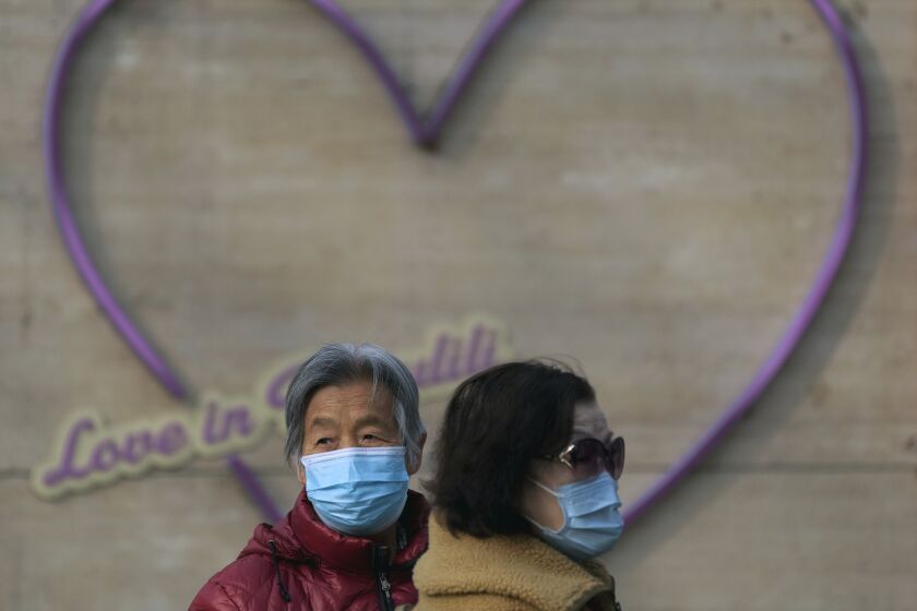 Dos mujeres con mascarilla se ven ante un adorno con forma de corazón en Beijing, el martes 22 de noviembre de 2022. (AP Foto/Andy Wong)