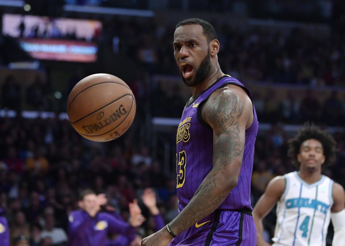 El alero LeBron James, izquierda, de los Lakers de Los Ángeles grita tras meter una volcada frente a los Hornets de Charlotte, el viernes 29 de marzo de 2019, en Los Ángeles. A la derecha está el base Devonte' Graham de los Hornets.