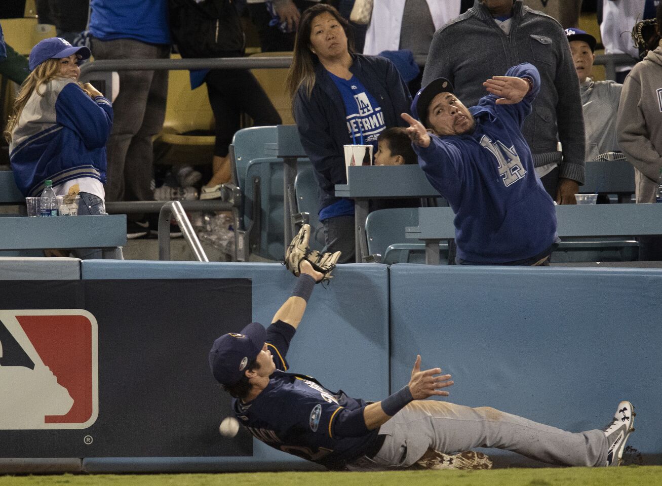 A fan almost interferes as Milwaukee Brewers right fielder Christian Yelich (22) tries to catch a foul ball hit by Dodgers Brian Dozier in the eighth inning.