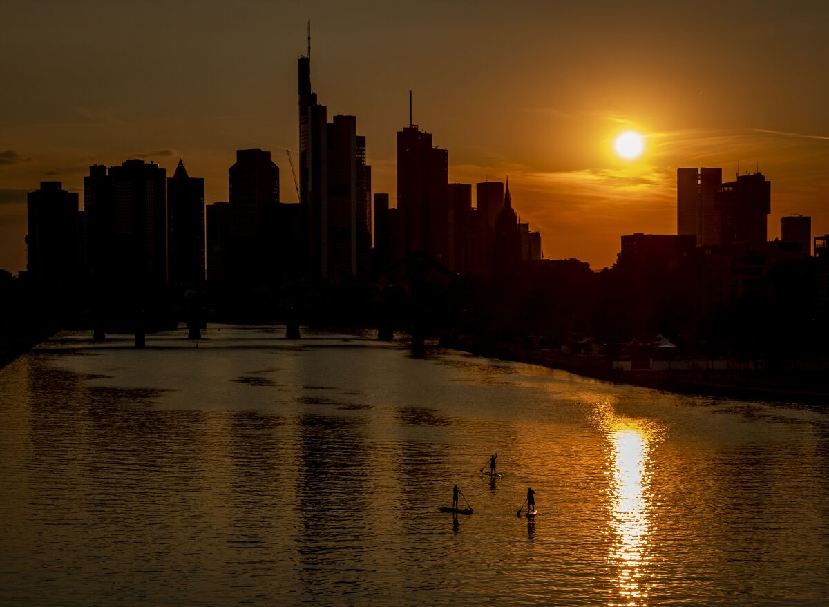 Three stand up paddlers on the river Main in Frankfurt, Germany, as the sun sets, Tuesday, Aug. 4, 2020. (AP Photo/Michael Probst)