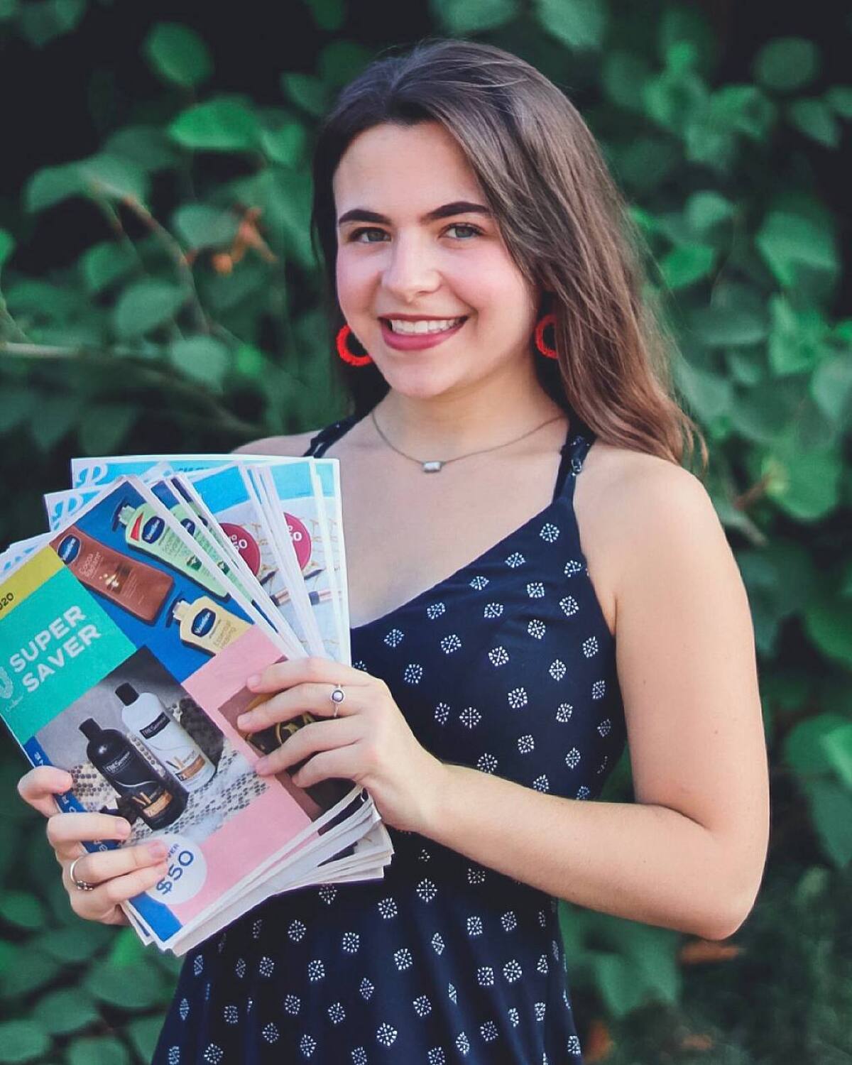 Social media influencer Julia Belkin poses with coupons in front of a wall of greenery.