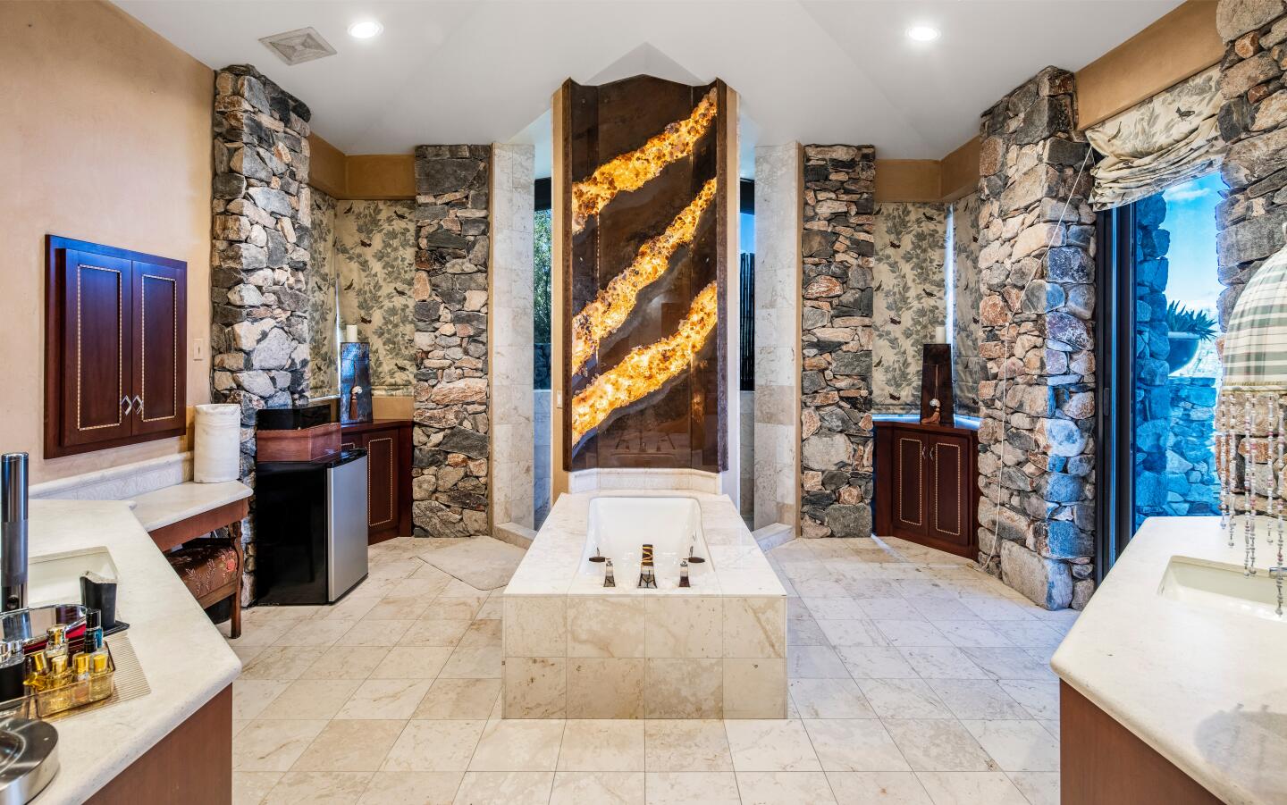 The bathroom has stone flooring and walls with windows and a bathtub