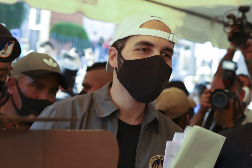 A man in a black mask and white cap worn backward is surrounded by other people