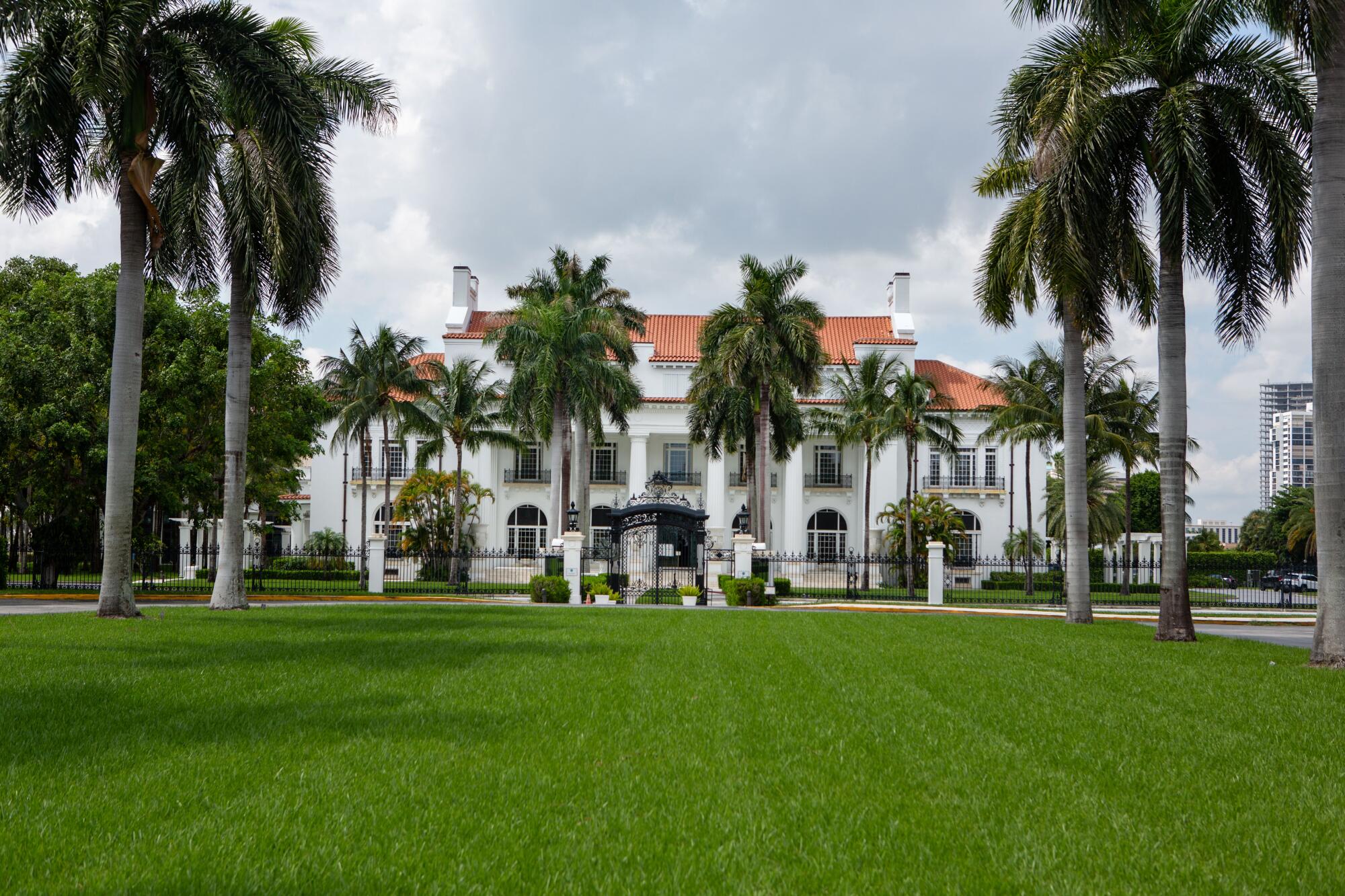A white mansion known with a large green lawn and palm trees