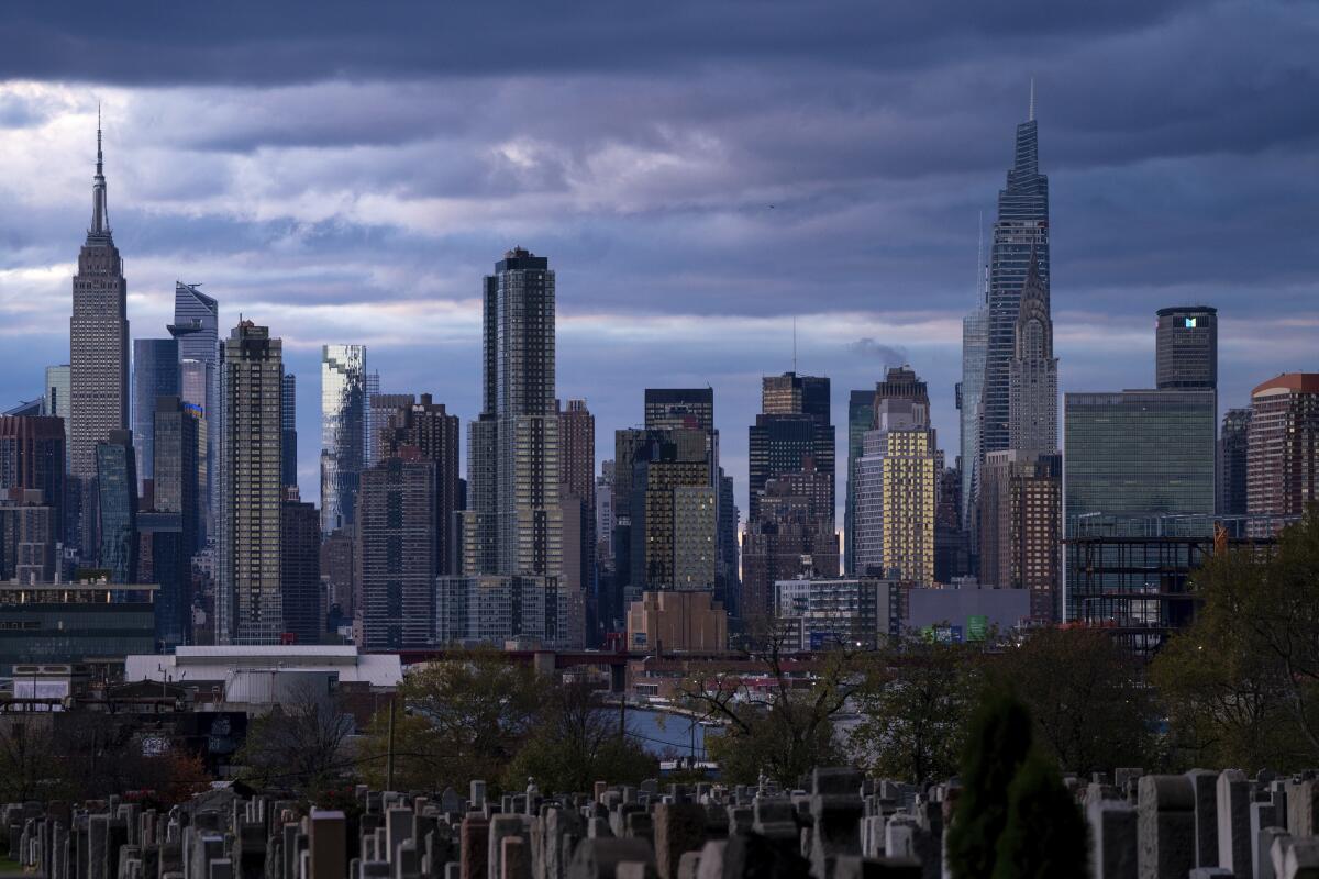 The sun sets behind the New York skyline, Sunday, Nov. 13, 2022, as seen from Calvary Cemetery. 