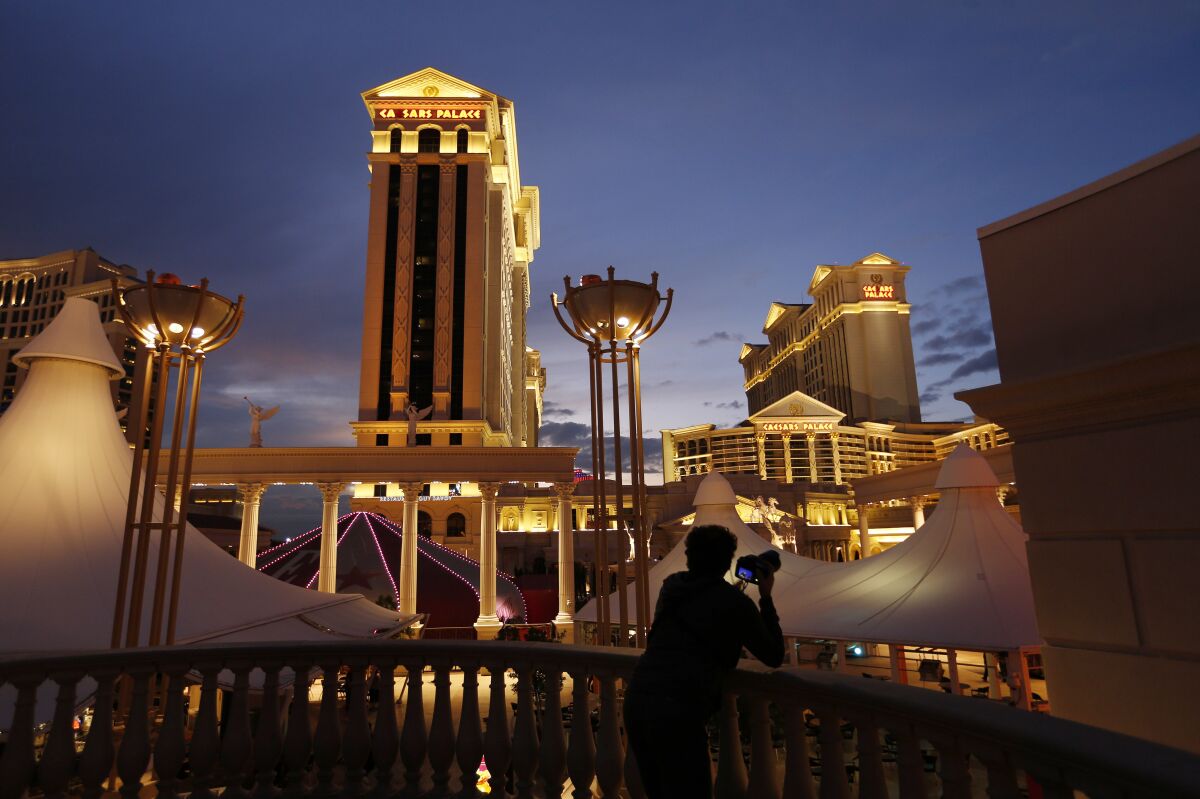 FILE - In this Jan. 12, 2015, file photo, a man takes pictures of Caesars Palace hotel and casino in Las Vegas. Caesars Entertainment and the company that produces the show "Absinthe" in Las Vegas are teaming up on theater and dining projects in three states that will cost nearly $100 million. Caesars says it has signed a deal with Spiegelworld to create new live theater projects at casinos in Las Vegas, Atlantic City and New Orleans. (AP Photo/John Locher, File)