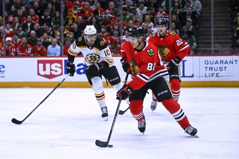 Chicago Blackhawks defenseman Caleb Jones (82) moves the puck away from Boston Bruins left wing A.J. Greer (10) during the first period of an NHL hockey game Tuesday, March 14, 2023, in Chicago. (AP Photo/Matt Marton)