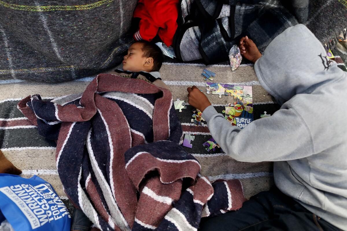 Gustavo Guinak, 2, sleeps as his brother Wilson Guinak, 13, works on a puzzle Tuesday in Tijuana. The family from Guatemala was among nearly 200 asylum seekers camped outside a U.S. port of entry this week.