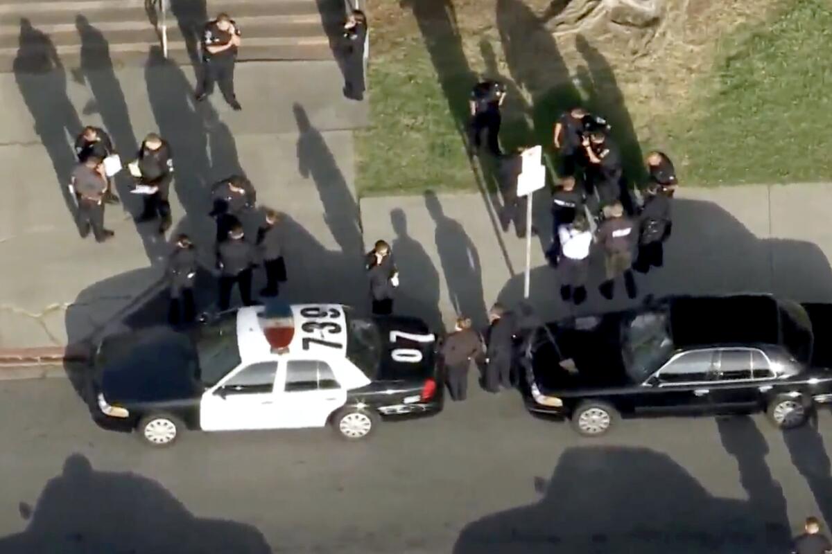 Aerial view of police officers standing on a sidewalk next to vehicles outside a school
