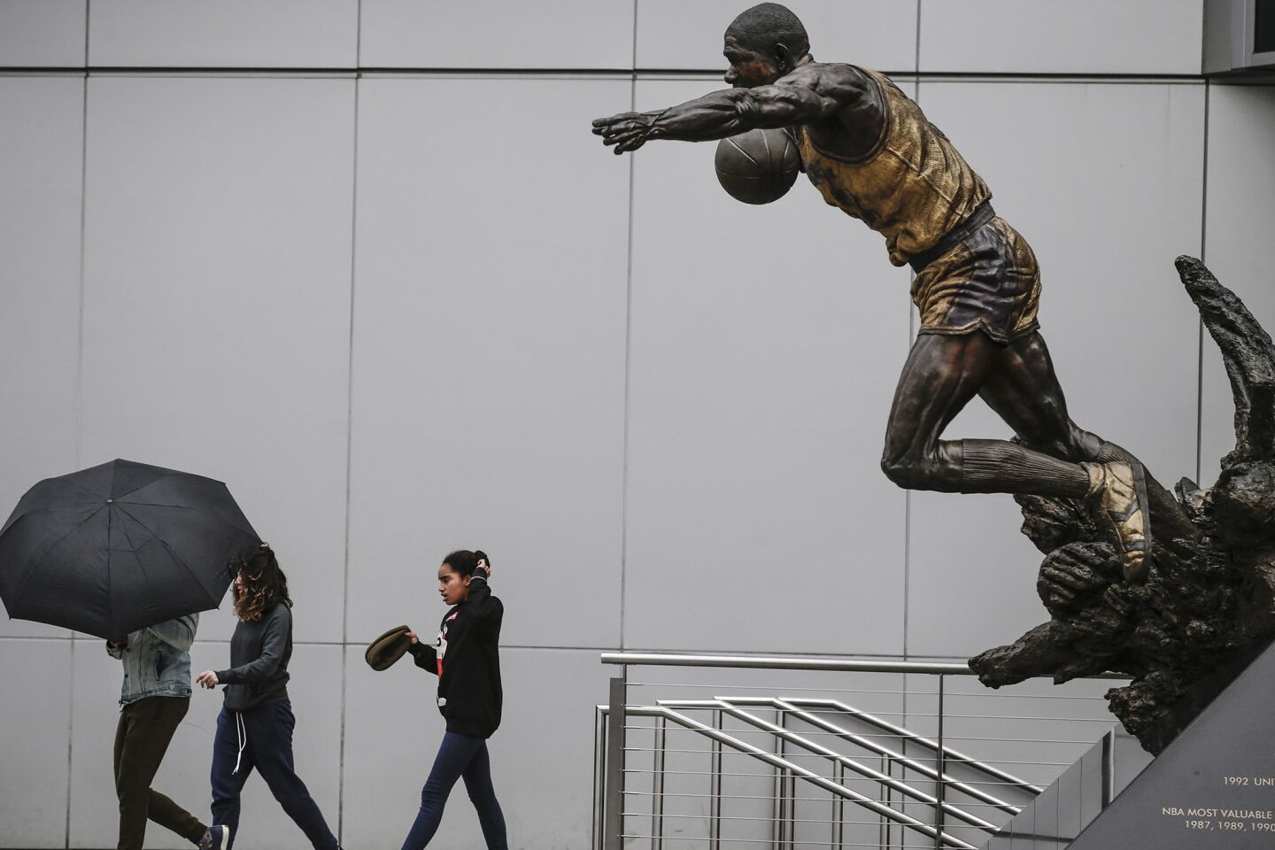 Pedestrians pass a statue of Magic Johnson leaning into a blustery wind outside Staples Center in downtown Los Angeles on Wednesday.