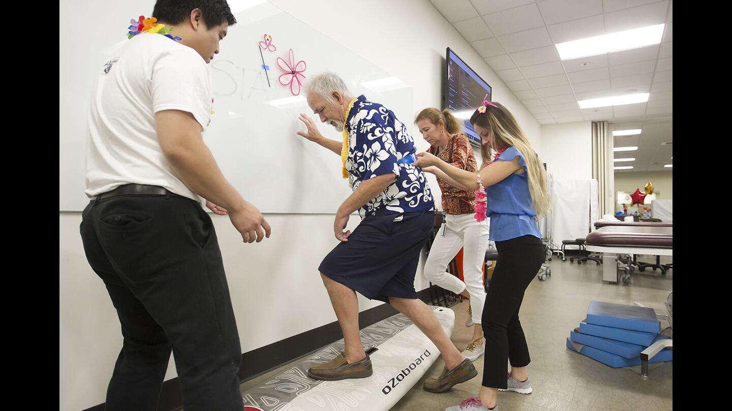 Boot camp participant Jim Eklund, 66, uses a surfboard to test his balance with the help of physical therapy students Salvador Abiera, left, and Bettina Nagy, far right, during the Chapman University department of physical therapy's annual boot camp at the Rinker Health Science Campus in Irvine.