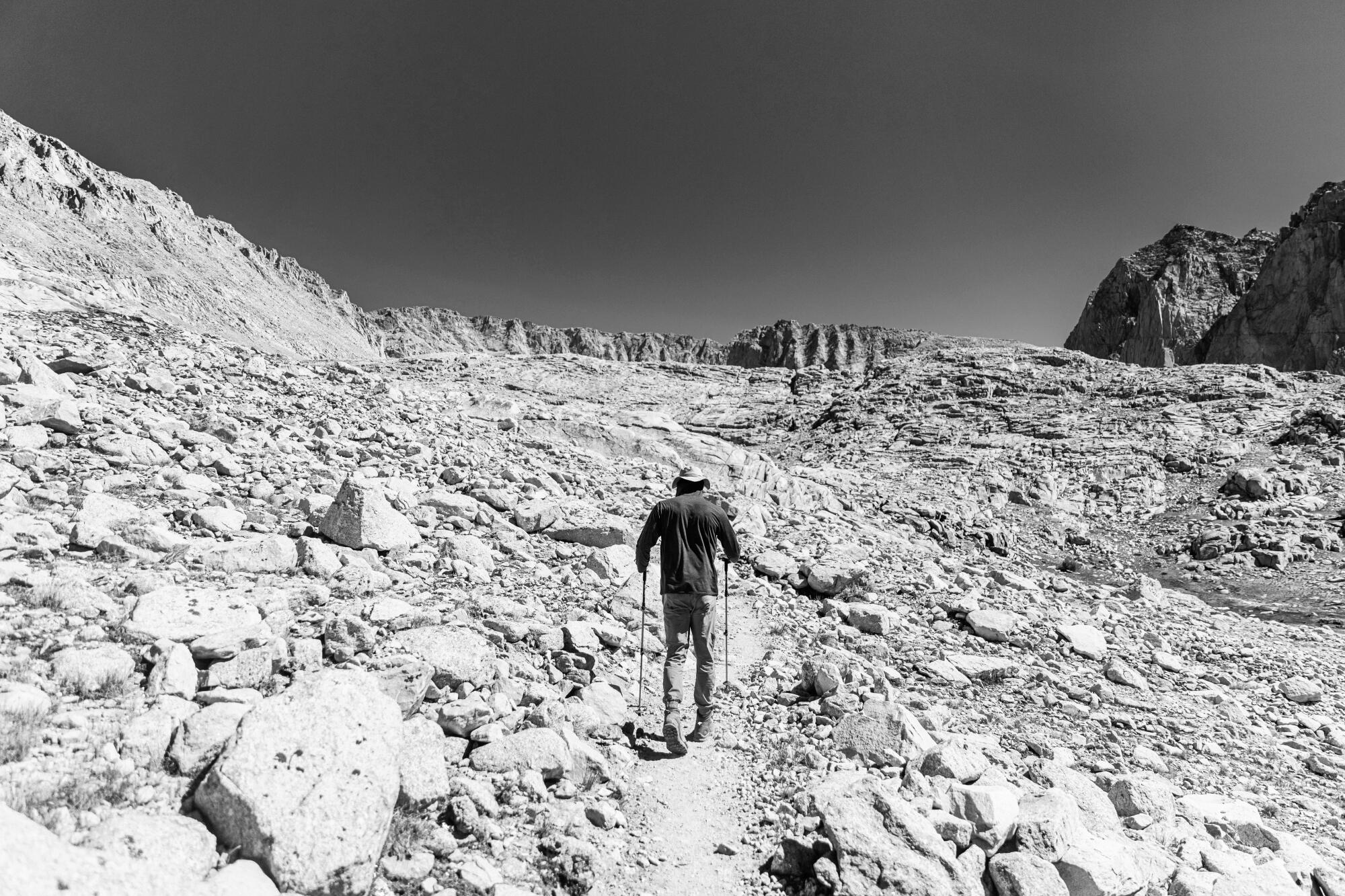 A man uses poles to walk through rocks up a mountain.