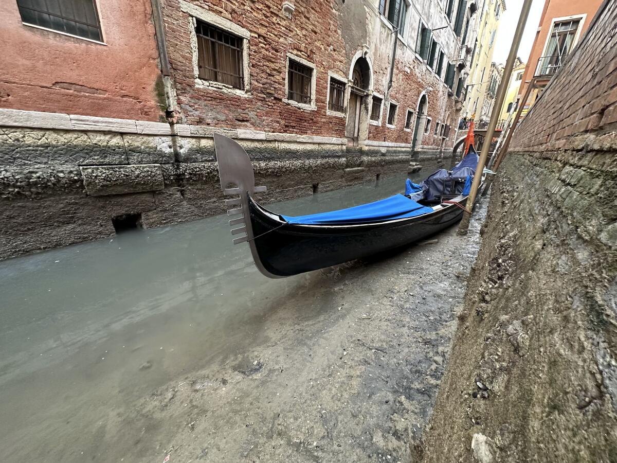 A gondola sits in a channel between brick buildings 
