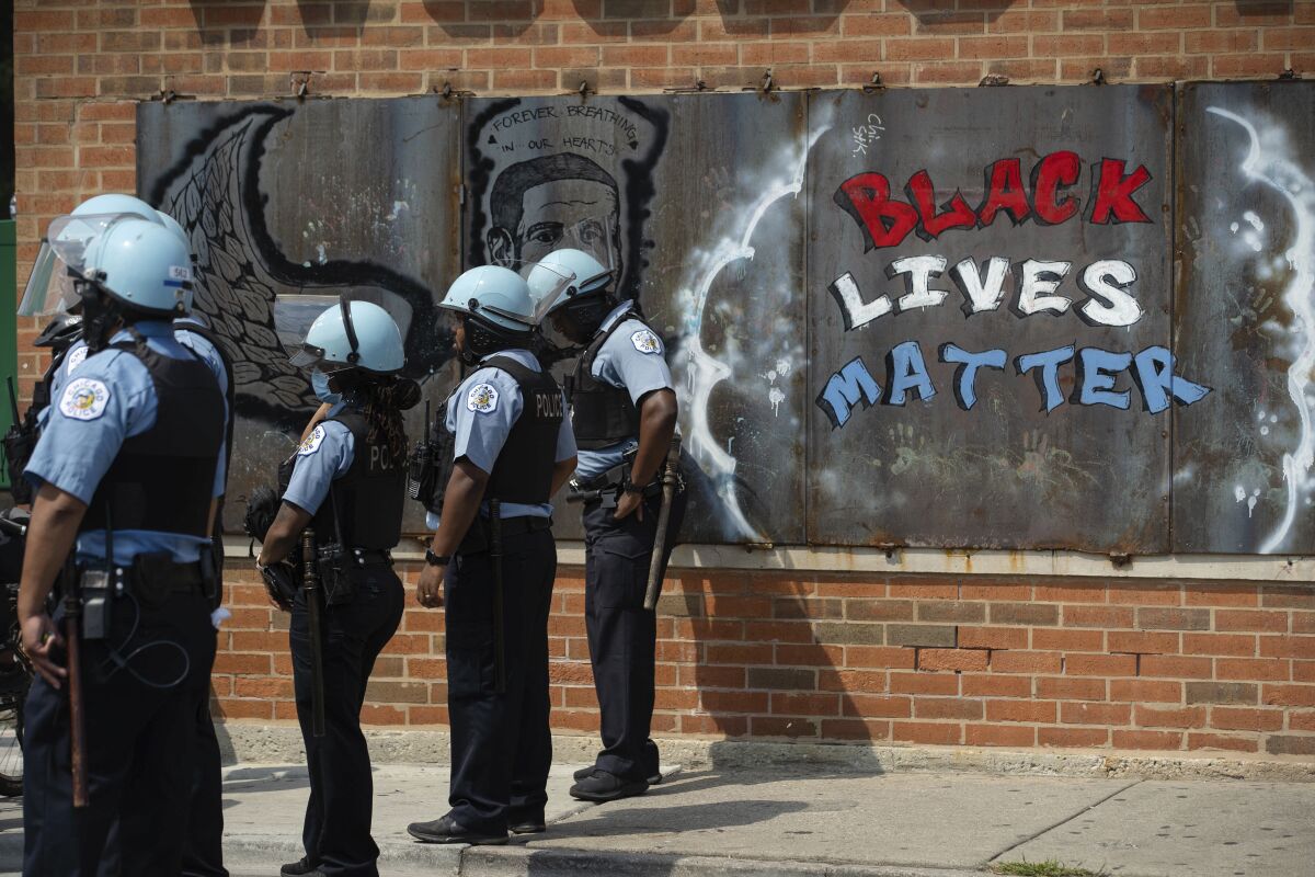 Police officers stand beside a mural for George Floyd 