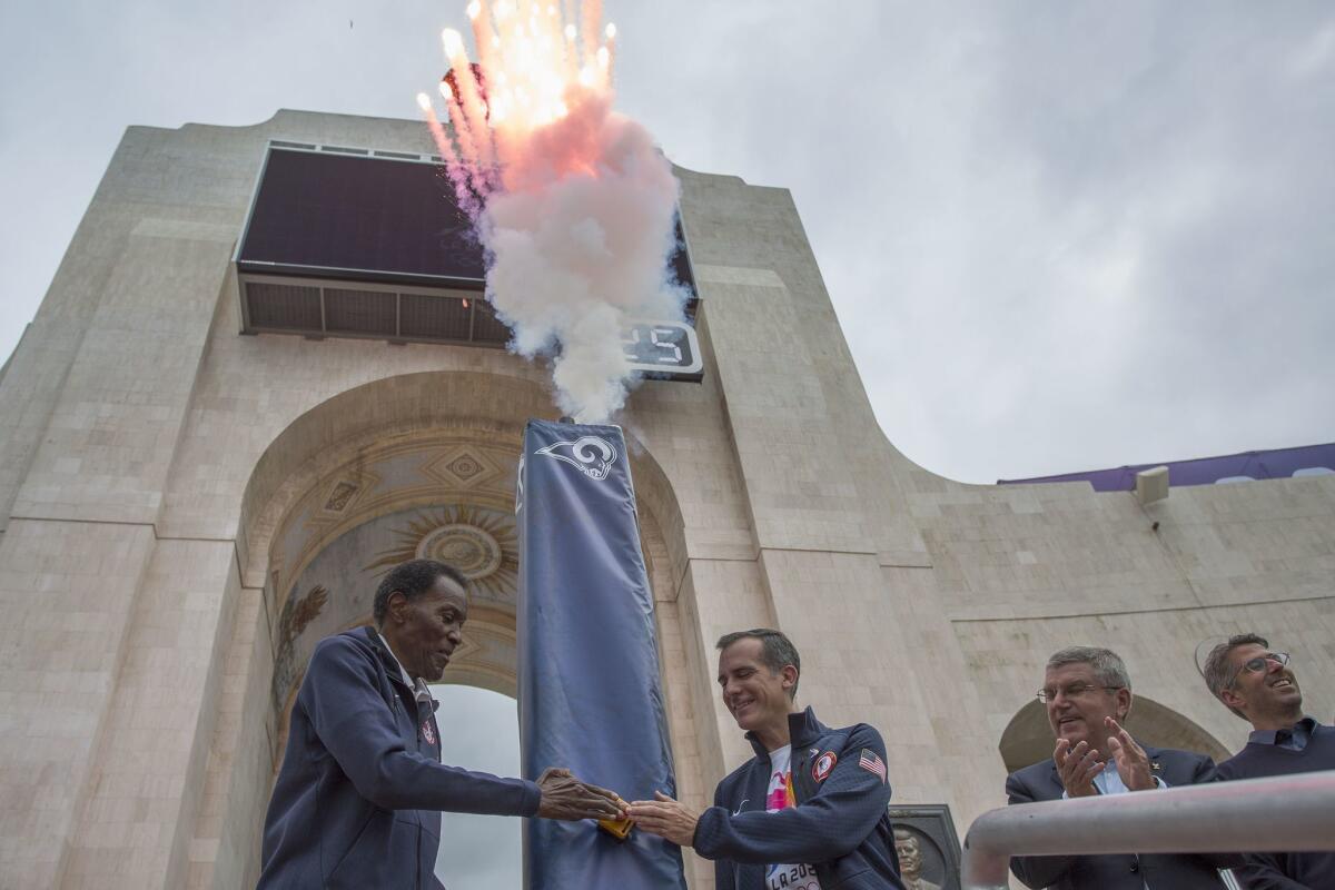 Olympic gold medalist Rafer Johnson (L), Los Angeles Mayor Eric Garcetti push the ignition switch to light the Los Angeles Memorial Coliseum's Olympic Cauldron as International Olympic Committee President Thomas Bach and LA 2028 Chairman Casey Wasserman (R) stand by on September 17, 2017 in Los Angeles, California to celebrate the announcement that the city will host the 2028 Olympic and Paralympic Games.