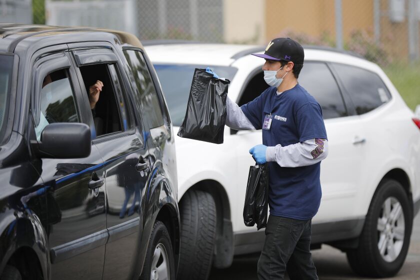 Austin Correia delivers a Chromebook to a Perry Elementary School parent waiting in a car at Morse High School on April 5, 2020. Morse High School served as a distribution hub for area schools as San Diego Unified started to distribute 40,000 of the laptops.
