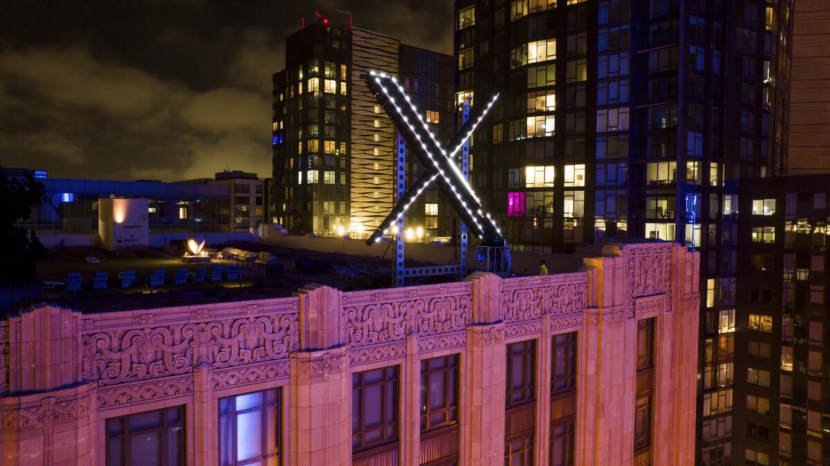 Workers install lighting on an "X" sign atop the company headquarters
