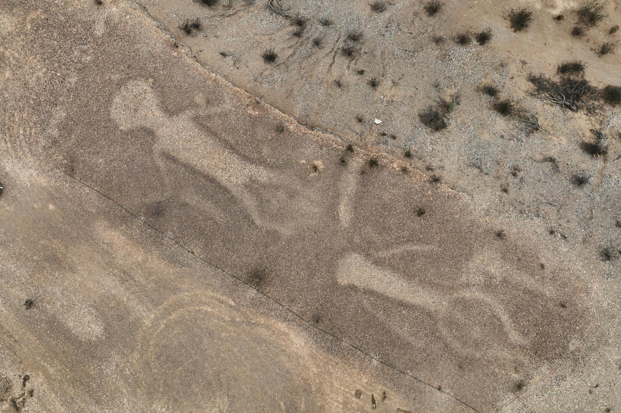 Images of two human forms are etched in the earth. 