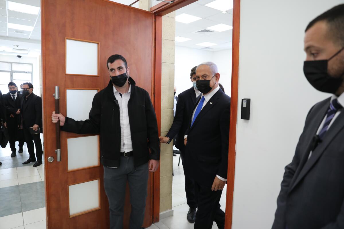 Benjamin Netanyahu and other men in face masks walk through a door. 