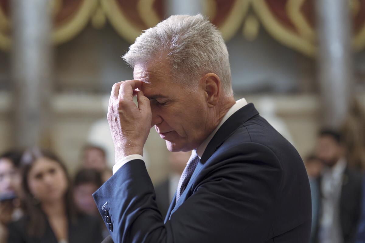 Kevin McCarthy holding a hand to his forehead and closing his eyes while standing in front of several people.