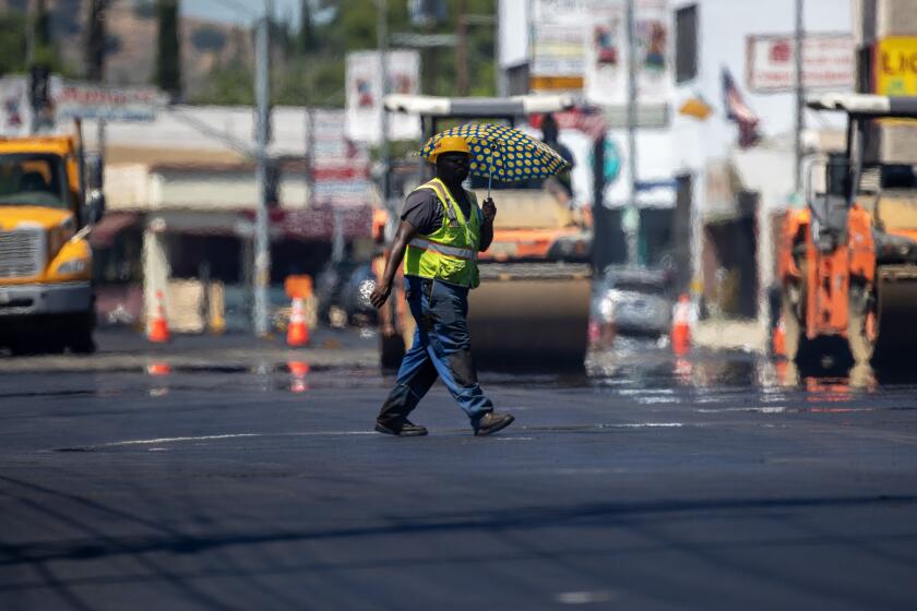 Woodland Hills, CA - July 27: Heat radiates up off fresh asphalt as a LA City street services worker carries an umbrella to ward off the sun as crews lay down new pavement on Ventura Blvd. on Thursday, July 27, 2023 in Woodland Hills, CA. (Brian van der Brug / Los Angeles Times)