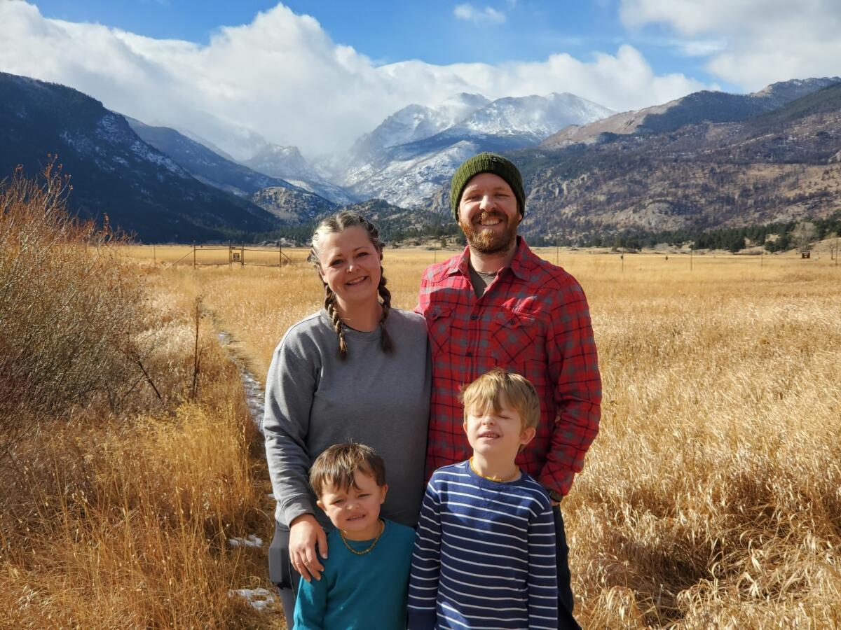 A man, woman and two small children stand in front of a field with mountains in the background.