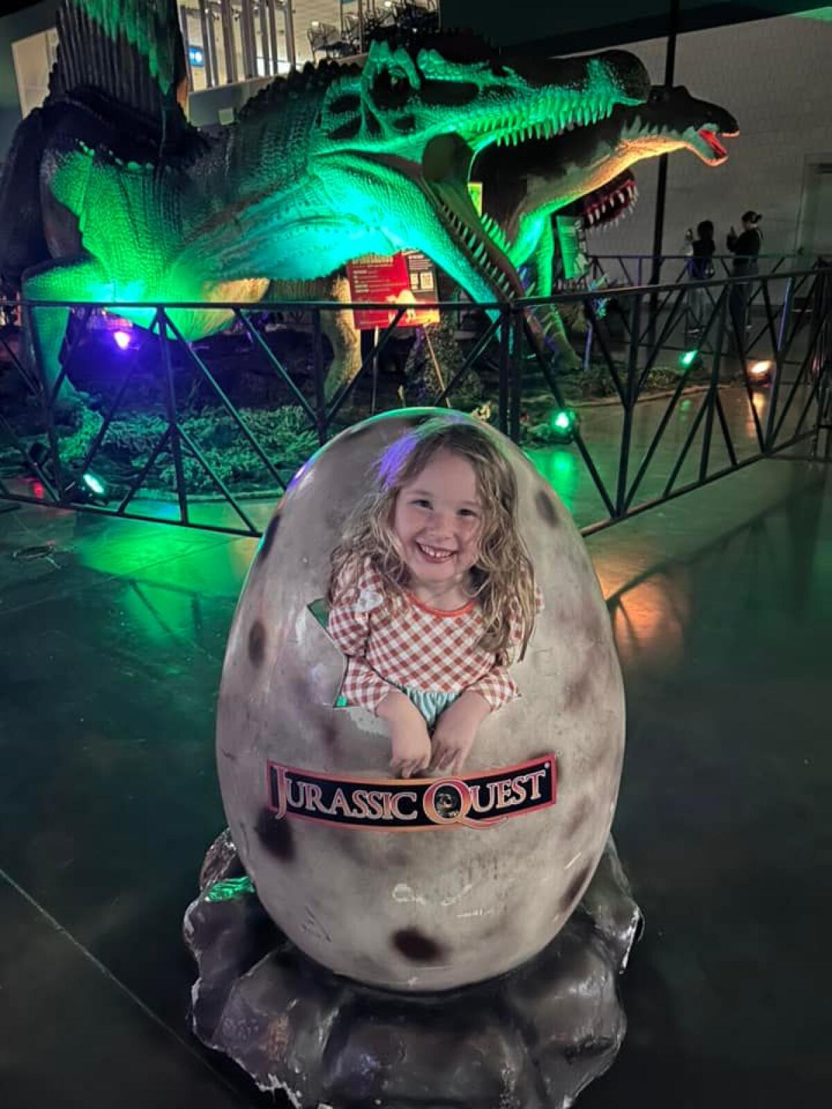 A young girl poses for a picture as though hatched from a dinosaur egg at a Jurassic Quest event.