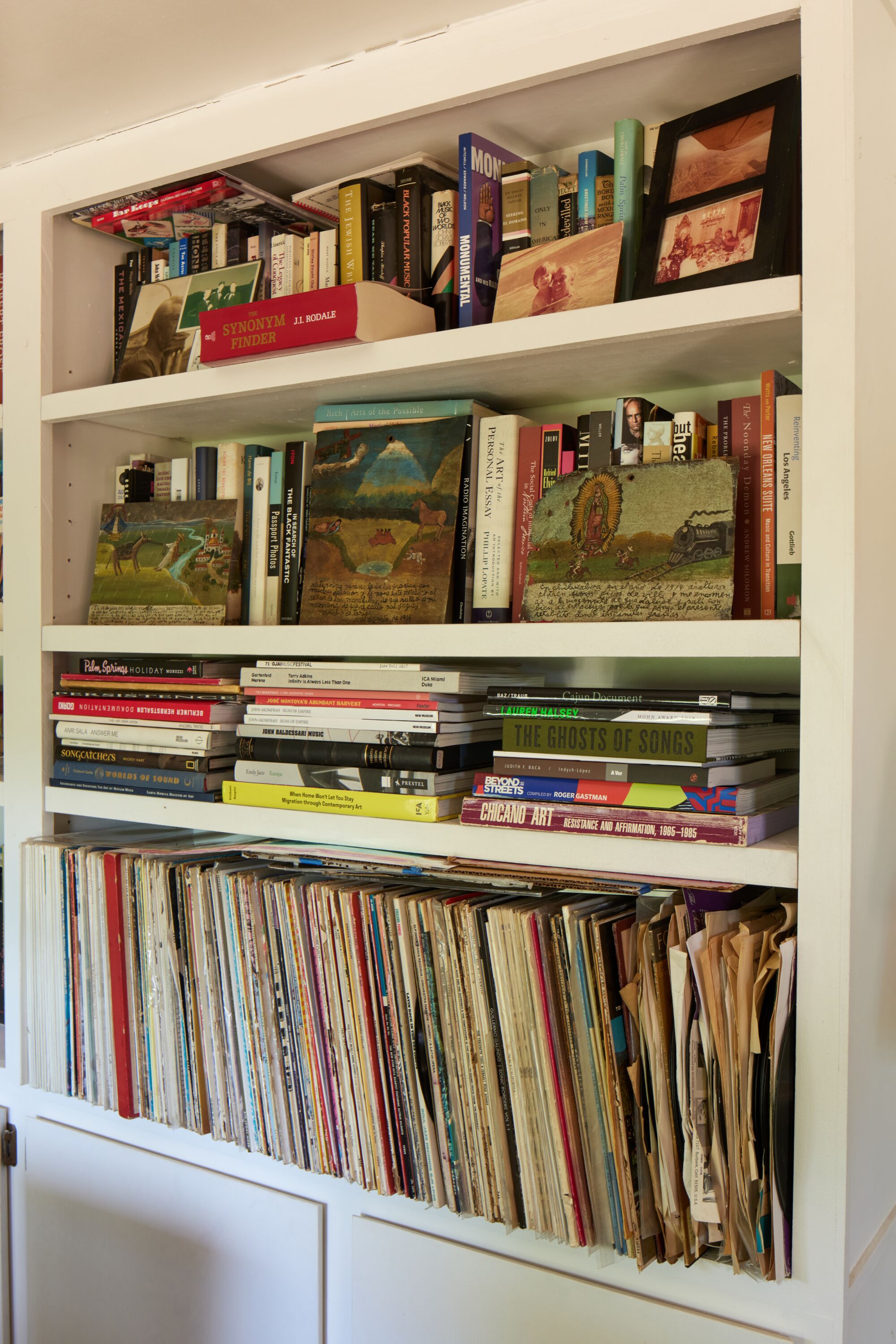 An image of a white bookshelf stuffed with books and with picture frames leaning against the books.