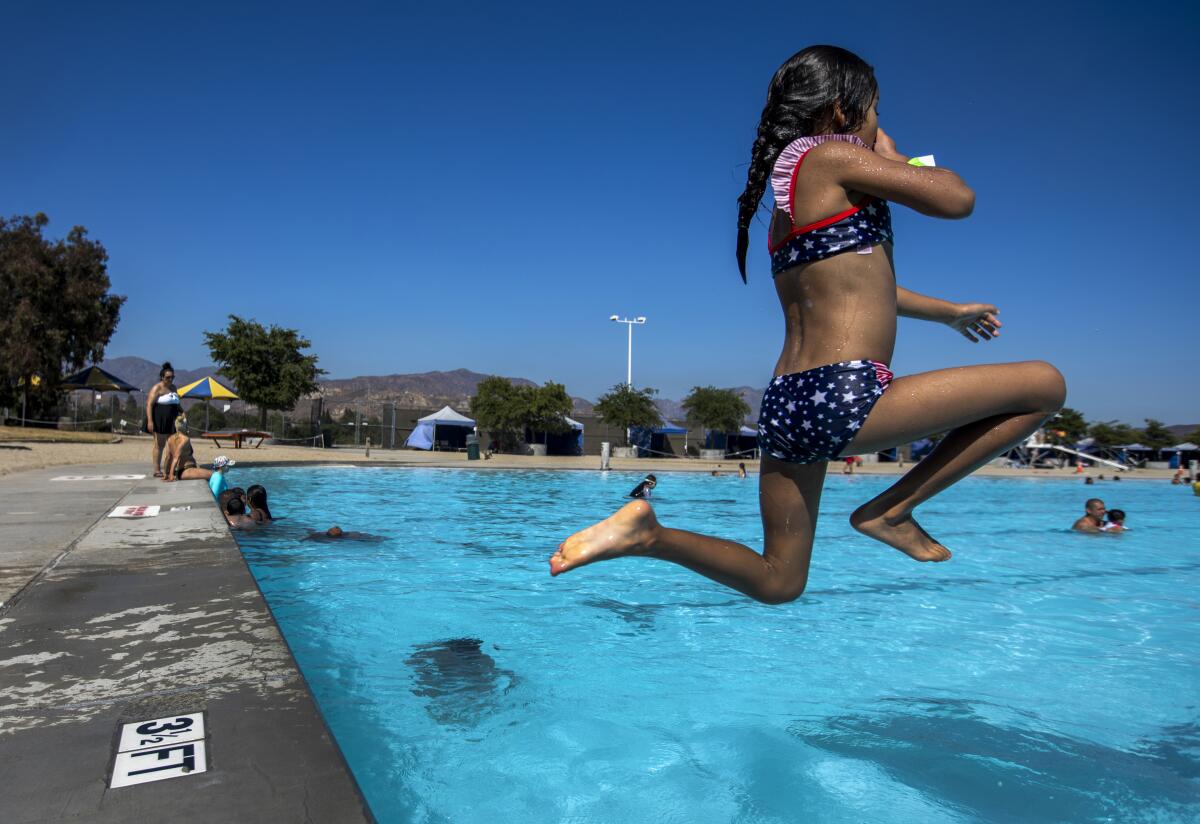A young girl in a two-piece suit holds her nose as she leaps into a pool.